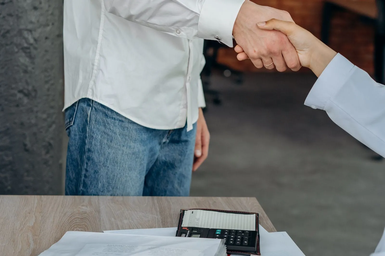 Duas pessoas apertam as mãos sobre uma mesa com calculadora e papéis