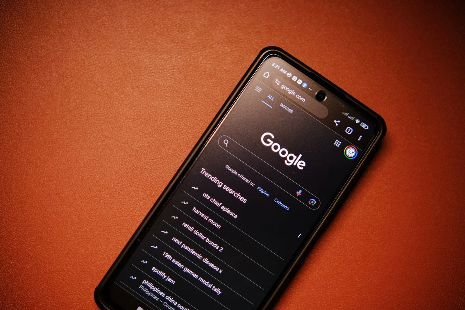 Celular sobre fundo laranja com a página de busca do Google aberta e uma lista de pesquisas