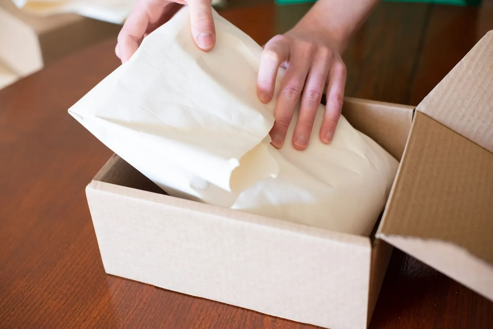 Mãos embalam um pedido em papel dentro de uma caixa de papelão